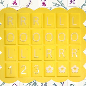 May include: A yellow tray with a scalloped edge holds 25 tiles. The tiles are yellow with white letters and numbers. The letters are R, L, and O. The numbers are 1, 2, and 3. There are also three white flower-shaped tiles.