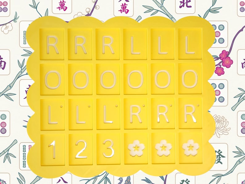 May include: A yellow tray with a scalloped edge holds 25 tiles. The tiles are yellow with white letters and numbers. The letters are R, L, and O. The numbers are 1, 2, and 3. There are also three flower-shaped tiles.
