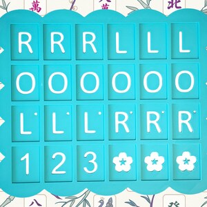 May include: A turquoise-colored game piece holder with white letters and numbers. The holder has a scalloped edge and contains the letters R, L, and O, along with the numbers 1, 2, and 3, and three flower symbols. The background has a floral pattern.