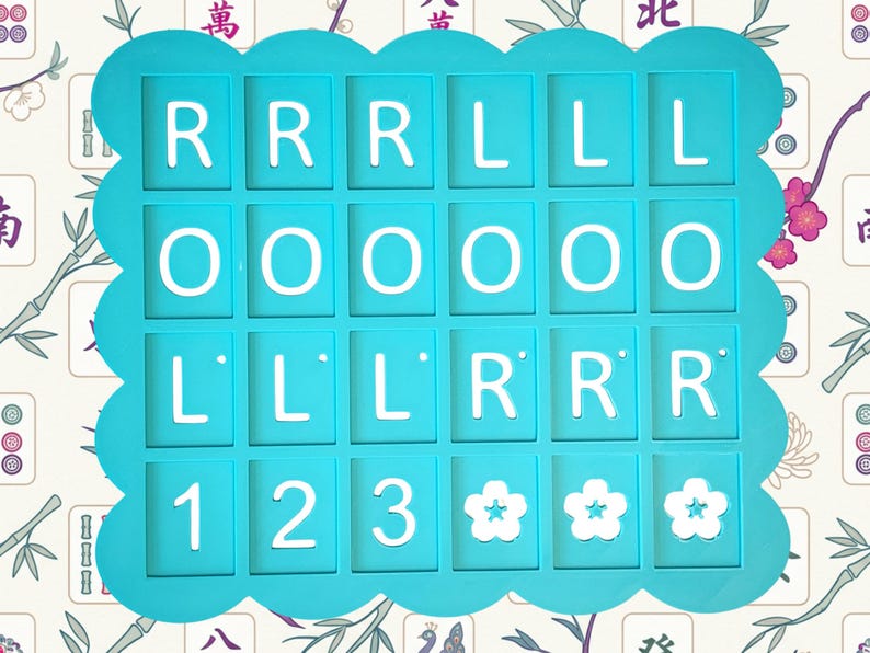 May include: A turquoise-colored game piece holder with white letters and numbers. The holder has a scalloped edge and contains the letters R, L, and O, along with the numbers 1, 2, and 3, and three flower symbols. The background has a floral pattern.