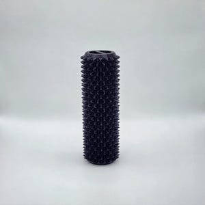 May include: A dark purple, cylindrical object with a textured surface of evenly spaced, conical spikes. The top rim has a decorative, ridged design. The object is set against a plain white background.