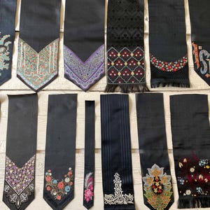 May include: A collection of black neckties with various embroidered and patterned designs. Some ties feature floral, paisley, or geometric patterns in colors like blue, red, and gold. Others are plain or have subtle textures.