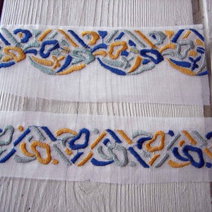 May include: Two pieces of white fabric with blue, gold, and silver embroidery. The embroidery is a repeating pattern of abstract shapes.