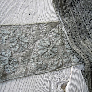 May include: Two pieces of green lace fabric, one with a floral pattern and the other with a more open weave, are laid out on a white wooden surface.