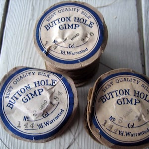 May include: Three spools of thread labeled "Best Quality Silk Button Hole Gimp" with different color numbers and yardage. The spools are brown with blue labels and white text.