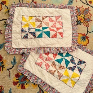 May include: Two white quilted pillow covers with colorful pinwheel designs. Each pillow has a ruffled edge with red, white, and blue stripes. The pinwheels are in shades of yellow, teal, red, and blue floral patterns.