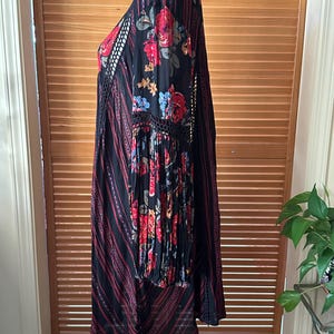 May include: Black dress with red floral print on the sleeves and bodice. The dress features a V-neck, long sleeves, and a striped pattern with red accents. The dress has a bohemian style.