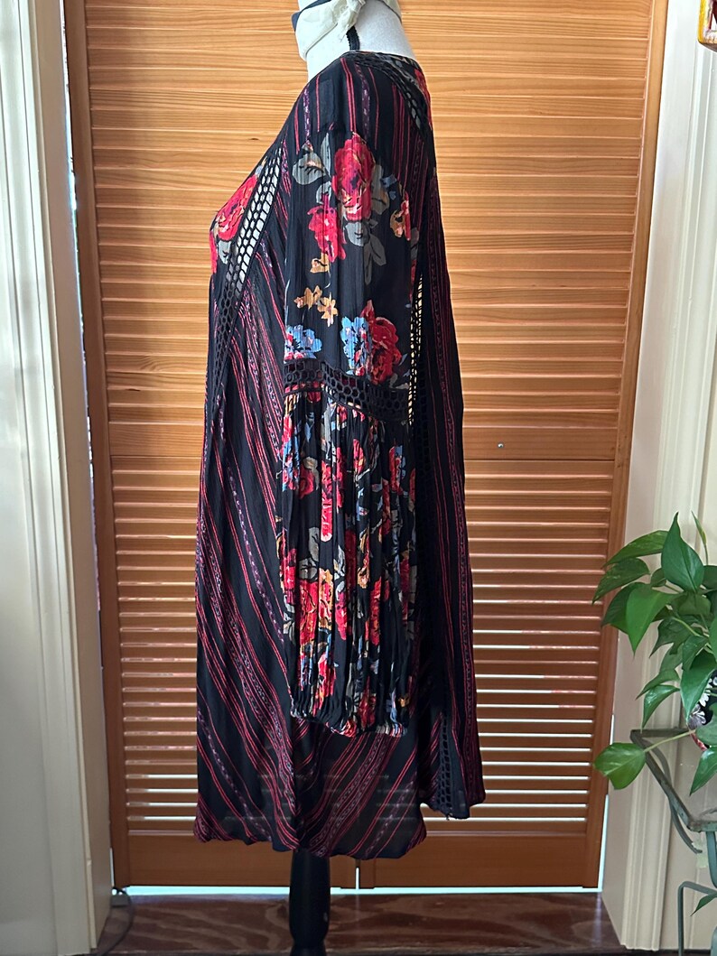 May include: Black dress with red floral print on the sleeves and bodice. The dress features a V-neck, long sleeves, and a striped pattern with red accents. The dress has a bohemian style.