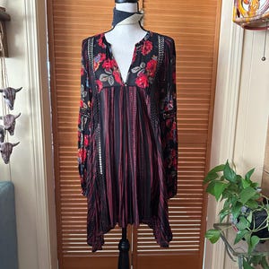 May include: Black tunic dress with red floral print and vertical red stripes. The long-sleeved dress features a V-neck and lace detailing on the sleeves and neckline. The dress is displayed on a black mannequin.