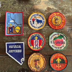 May include: A collection of vintage Jaycees patches, featuring various designs and locations. Patches include the state of Idaho, Nevada, and cities like Minneapolis, Atlanta, and San Diego. The patches are in various shapes and colors.