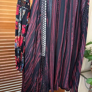 May include: Black dress with red vertical stripes and floral patterned sleeves. The dress features a lace-like design on the sides and sleeves. The sleeves have a floral pattern with red, blue, and yellow flowers.