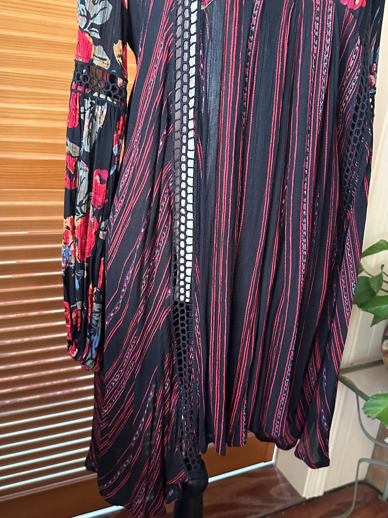 May include: Black dress with red vertical stripes and floral patterned sleeves. The dress features a lace-like design on the sides and sleeves. The sleeves have a floral pattern with red, blue, and yellow flowers.