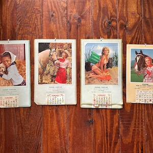 May include: Four vintage wall calendars featuring photographic prints of people with animals or in outdoor settings. Each calendar includes a small January date pad at the bottom and the text Ingrams Furniture printed below the main image.