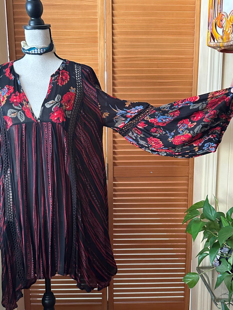 May include: Black dress with red and blue floral print sleeves and bodice. The dress has a V-neck and a striped pattern with red accents. The sleeves are long and flared, and the dress is displayed on a mannequin.