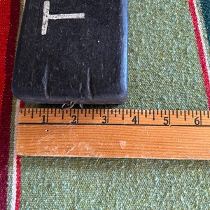 Op de afbeelding: Een donker, rechthoekig object met een witte "T"-vorm aan de bovenkant, naast een houten liniaal. De liniaal toont metingen in centimeters. Het object lijkt gemaakt van een donker, mogelijk houten materiaal.