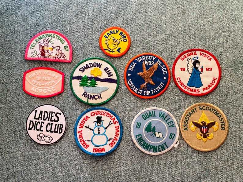 Op de afbeelding: Een verzameling geborduurde patches met diverse ontwerpen en tekst. Patches zijn onder meer "Telemarketing '87", "Early Bird", "Shadow Rim Ranch", "BSA Varsity 1993", "Sierra Vista Christmas Parade", "Ladies Dice Club" en "Assistant Scoutmaster".