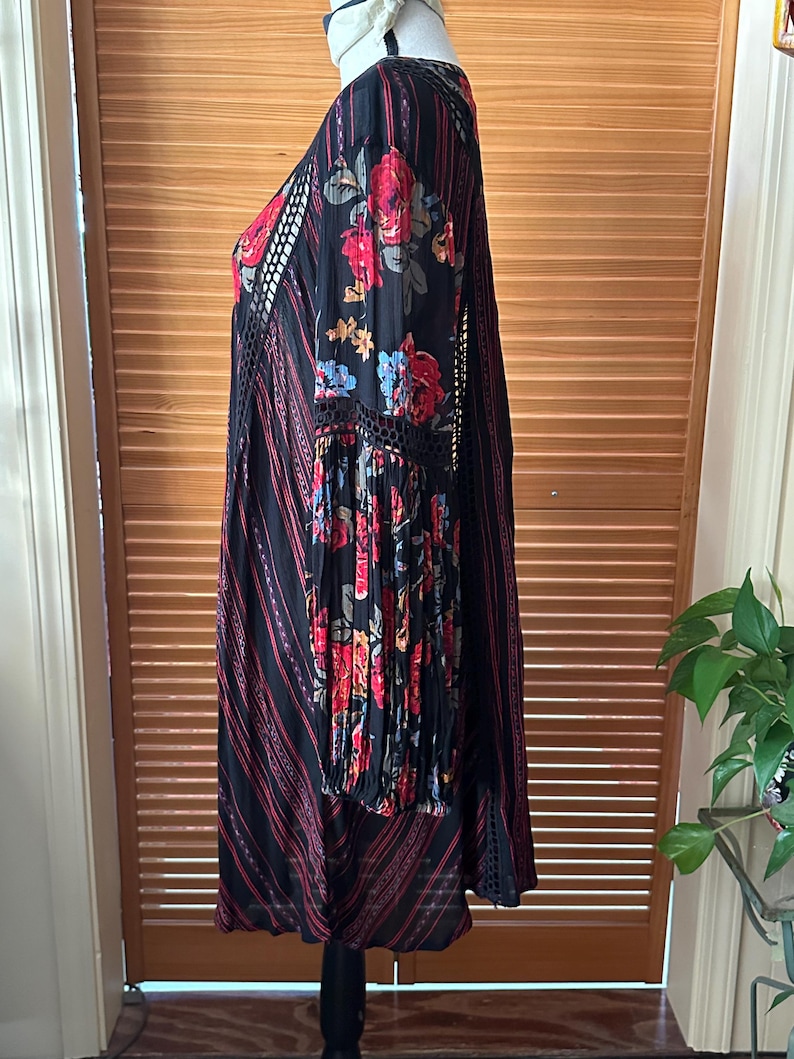 May include: Black dress with red floral print on the sleeves and bodice. The dress features a V-neck, long sleeves, and a striped pattern with red accents. The dress has a bohemian style.