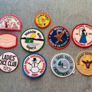 Op de afbeelding: Een verzameling geborduurde patches met diverse ontwerpen en tekst. Patches met opschriften als "Telemarketing '87", "Early Bird", "Shadow Rim Ranch", "BSA Varsity 1993", "Sierra Vista Christmas Parade", "Ladies Dice Club" en "Assistant Scoutmaster".