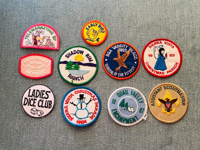 Op de afbeelding: Een verzameling geborduurde patches met diverse ontwerpen en tekst. Patches met opschriften als "Telemarketing '87", "Early Bird", "Shadow Rim Ranch", "BSA Varsity 1993", "Sierra Vista Christmas Parade", "Ladies Dice Club" en "Assistant Scoutmaster".