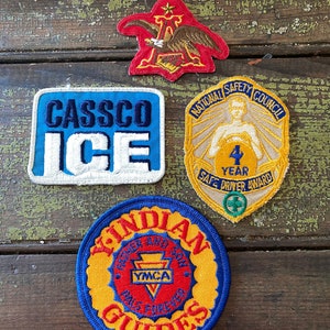 May include: A collection of vintage embroidered patches. Includes a red patch with an eagle, a blue and white "CASSCO ICE" patch, a yellow "National Safety Council 4 Year Safe Driver Award" patch, and a round "Indian Guides" patch.