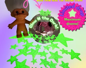 May include: A whimsical image featuring a vintage troll doll and a glowing, faceted sphere with the text "Glow N the Dark!" surrounded by neon green star shapes. The text "Limited Edition Earrings" and "Maximum drama!" are also visible.