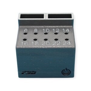 May include: A dark teal and gray drill bit holder with numbered holes from 6 to 24. The holder has two rectangular openings at the top and the text "F3D" on the front. A power symbol is also visible.