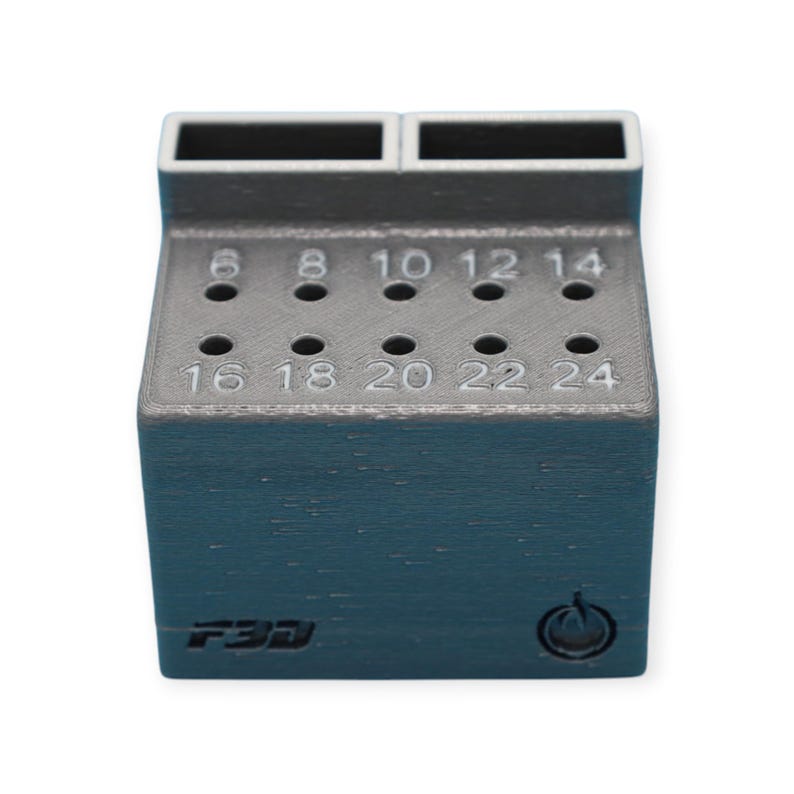 May include: A dark teal and gray drill bit holder with numbered holes from 6 to 24. The holder has two rectangular openings at the top and the text "F3D" on the front. A power symbol is also visible.
