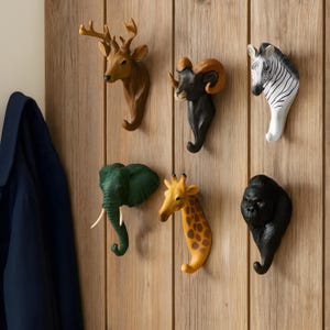 Könnte beinhalten: Eine Sammlung von Tier-Wandhaken. Die Haken zeigen einen Hirsch, einen Widder, ein Zebra, einen Elefanten, eine Giraffe und einen Gorilla. Jeder Haken hat eine andere Farbe und einen Haken unten.