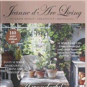 May include: The cover of Jeanne d'Arc Living magazine features a garden scene with a weathered wooden table, terracotta pots, and a white chair. Text includes '140 pages without ads', 'SUMMER DREAMS', 'TASTY SUMMER DISHES', and 'A wonderful SUMMER IN THE GARDEN'.