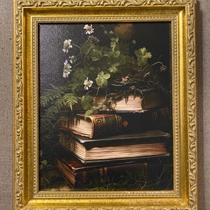 May include: A framed still life painting featuring a stack of antique books with dark green and brown covers. White flowers and green foliage are arranged on top of the books. The frame is ornate and gold-colored.