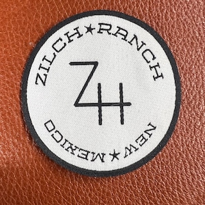 May include: A black and white circular patch with the text "Zilch Ranch New Mexico" and a star between "New" and "Mexico". The text "Zilch Ranch" is in a circular pattern around the number "74" in the center of the patch.