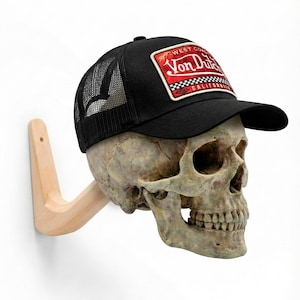 Può includere: Un cappellino da camionista nero con retro in rete e una toppa rossa e bianca con la scritta "Von Dutch California" è esposto su un teschio montato su una staffa di legno. Il cappello ha una visiera curva.