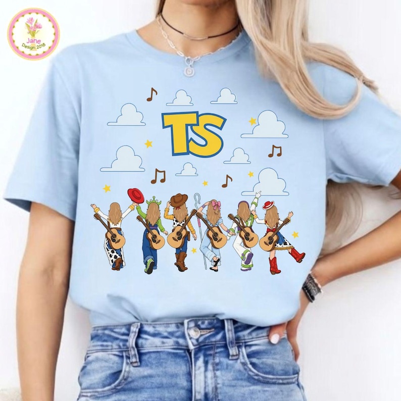 May include: A light blue t-shirt featuring a graphic print of six figures with long hair, each holding an acoustic guitar. The design includes white clouds, yellow stars, brown musical notes, and the large yellow text TS centered at the top.