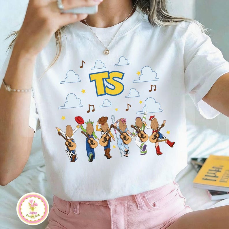May include: A white short-sleeve t-shirt featuring a graphic print of six cartoon figures with long hair, each holding a guitar. Above them are blue clouds, yellow stars, musical notes, and the large yellow text TS with a blue outline.