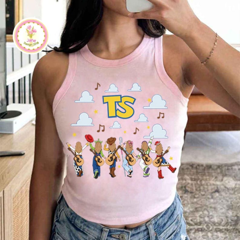 May include: A light pink sleeveless tank top featuring a graphic print of six cartoon figures playing acoustic guitars. Above the figures are white clouds, musical notes, and the yellow text TS with a blue outline. The top has a ribbed neckline.