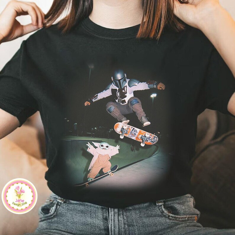 May include: Black t-shirt featuring a graphic of a character in a helmet skateboarding above a ramp, with a smaller character on a skateboard below. The design includes a skateboard with an orange and white design.
