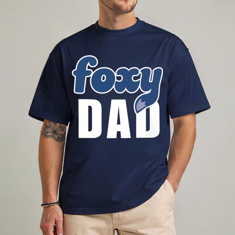 K&ouml;nnte beinhalten: Marineblaues T-Shirt mit dem Schriftzug "foxy DAD" in Wei&szlig; und Blau. Das Wort "foxy" hat einen blauen Fuchsschwanz. Das T-Shirt hat einen l&auml;ssigen Stil.