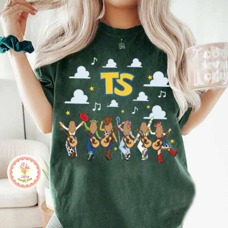 May include: A dark green short-sleeve t-shirt featuring a graphic print of six figures with long blonde hair holding acoustic guitars. The design includes white clouds, yellow stars, musical notes, and the large yellow text TS in a bold font.