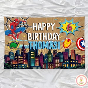 May include: A colorful birthday banner featuring the text "HAPPY BIRTHDAY THOMAS!" with a cityscape backdrop. Includes illustrations of Spider-Man, the Hulk's fist, Iron Man's helmet, and Captain America's shield. A large number 6 is also displayed.