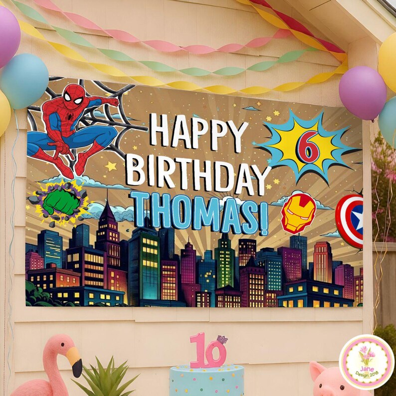 May include: A birthday banner featuring Spider-Man, the text "Happy Birthday Thomas!", and the number 6 in a comic book style. The banner also includes city skyline graphics and superhero emblems. Balloons and a cake are also visible.