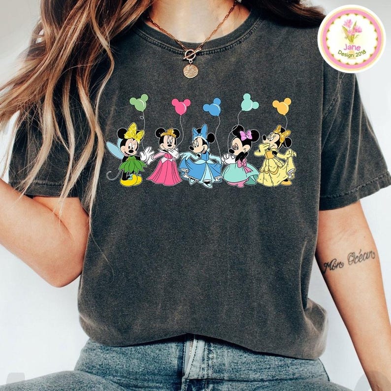 May include: Dark gray t-shirt featuring a colorful graphic of five cartoon mice holding balloons. Each mouse is dressed in a different outfit and holding a balloon of a matching color. The shirt has a vintage, worn look.