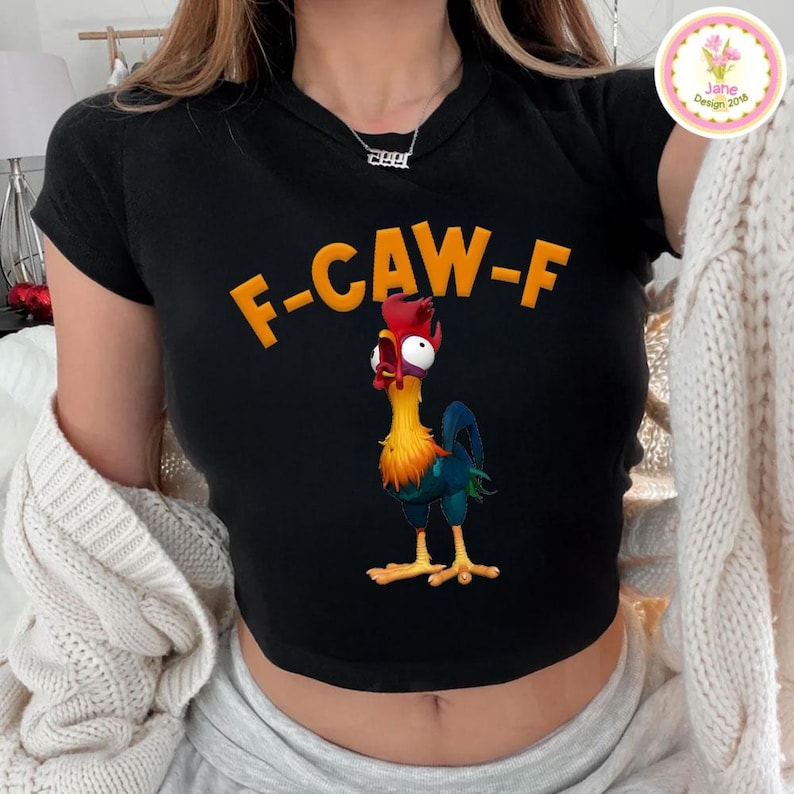 以下が含まれることがあります： オレンジ色の「F-CAW-F」の文字と漫画のニワトリのイラストが描かれた黒いクロップドトップス。ニワトリは赤、黄、青、緑色です。このトップスは半袖です。