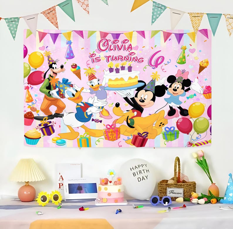 Puede incluir: Una pancarta rosa de cumplea&ntilde;os con personajes de Disney como Mickey Mouse, Minnie Mouse, Donald Duck y Goofy. La pancarta dice "Olivia cumple 6 a&ntilde;os" e incluye globos, regalos y una tarta. Las decoraciones de la fiesta est&aacute;n dispuestas sobre una mesa.