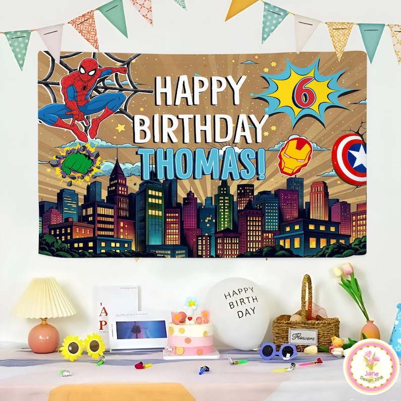 May include: A birthday banner featuring Spider-Man, the text "HAPPY BIRTHDAY THOMAS!", and a cityscape. The banner also includes the number 6, Iron Man's mask, and Captain America's shield. Party decorations are on a table.