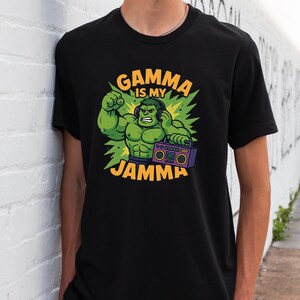 May include: Black t-shirt with a green cartoon character wearing headphones and holding a boombox. The text "GAMMA IS MY JAMMA" is in yellow and green. The character is flexing a green arm.