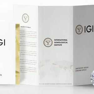 K&ouml;nnte beinhalten: Ein facettierter Diamant neben einer wei&szlig;en Brosch&uuml;re und einem gefalteten Bericht. Die Brosch&uuml;re und der Bericht zeigen das IGI-Logo und Text, darunter "Laboratory Grown Diamond Report" und "International Gemological Institute."