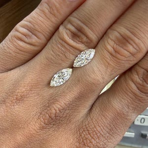 K&ouml;nnte beinhalten: Zwei Diamanten im Marquiseschliff, jeweils mit mehreren Facetten, werden gezeigt. Die Diamanten sind vor einem neutralen Hintergrund platziert, der ihre Brillanz hervorhebt. Die l&auml;ngliche Form der Diamanten ist ein wichtiges Merkmal, das Licht reflektiert und einen funkelnden Effekt erzeugt.