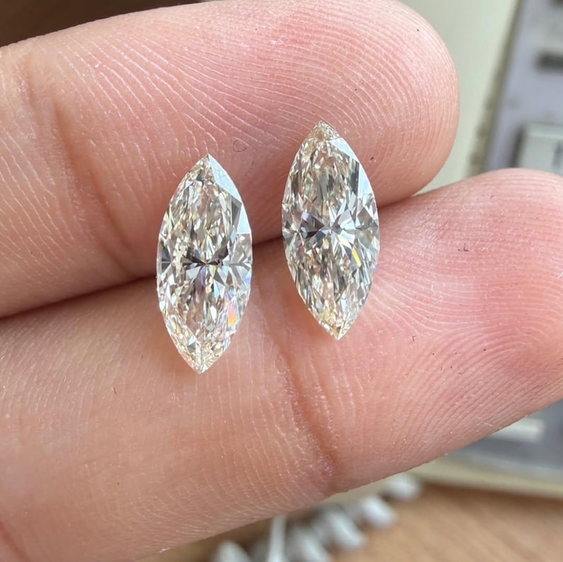 K&ouml;nnte beinhalten: Zwei Diamanten im Marquiseschliff mit einem warmen Champagnerton. Die Edelsteine werden zwischen den Fingern gehalten und zeigen ihre l&auml;ngliche Form und die brillanten Facetten. Die Diamanten sind wahrscheinlich f&uuml;r die Schmuckherstellung.