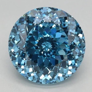 May include: A round, faceted gemstone with a brilliant cut. The gem displays a range of blue hues, from light to deep shades, creating a sparkling effect. The facets reflect light, giving the stone a captivating appearance. The gemstone is set against a neutral background.