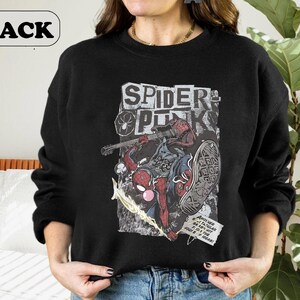 Peut inclure: Sweat-shirt noir avec un motif Spider-Man et l'inscription "SPIDER PUNK" dans une police de caract&egrave;res us&eacute;e. Le motif comprend une guitare et une bulle de dialogue. Le mot "BLACK" est dans un ovale blanc en haut &agrave; gauche.